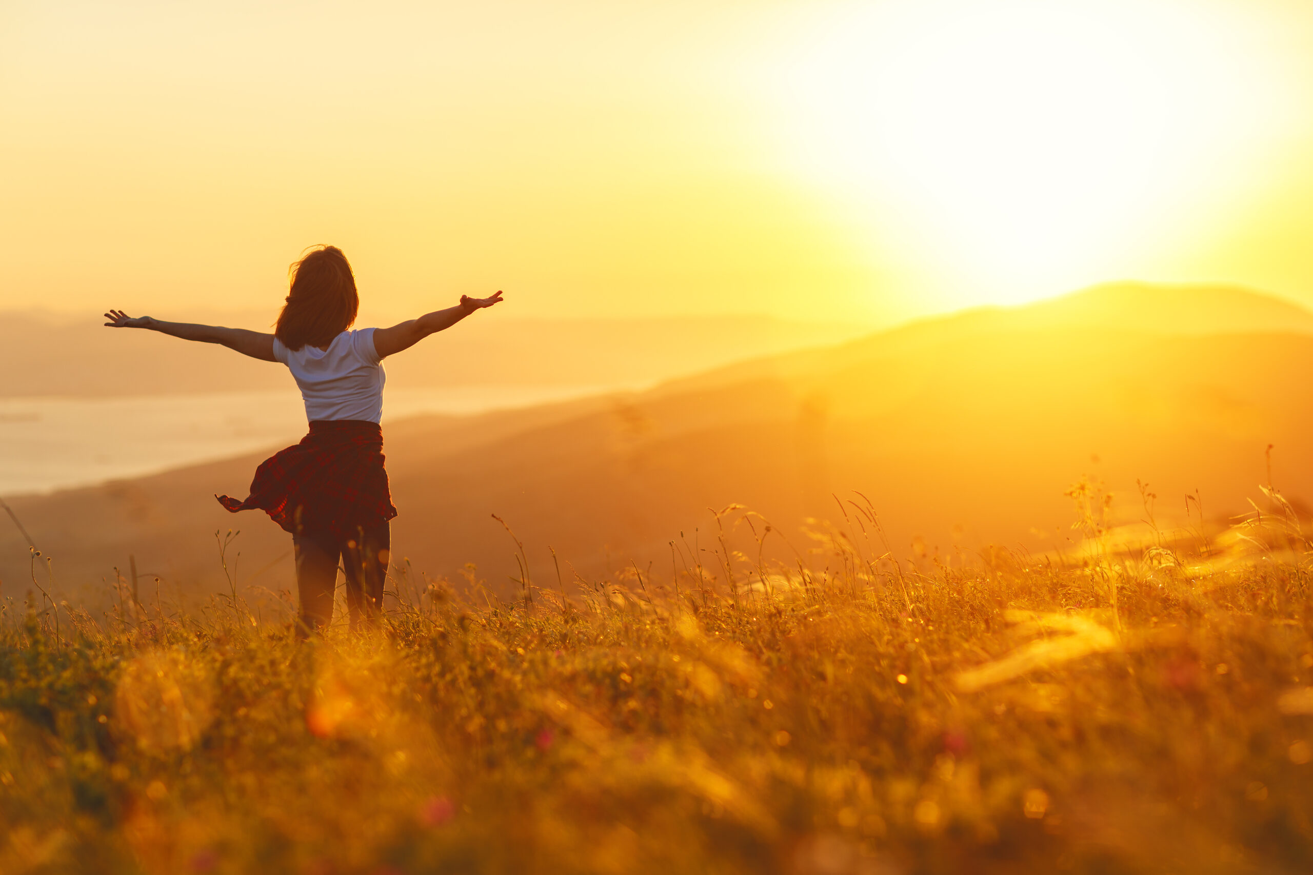 Happy woman standing with her back on sunset in nature iwith open hands